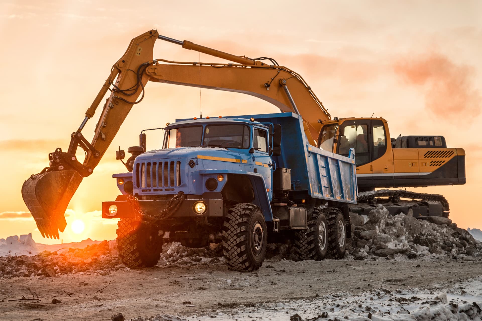 Heavy truck and excavator working at sunset